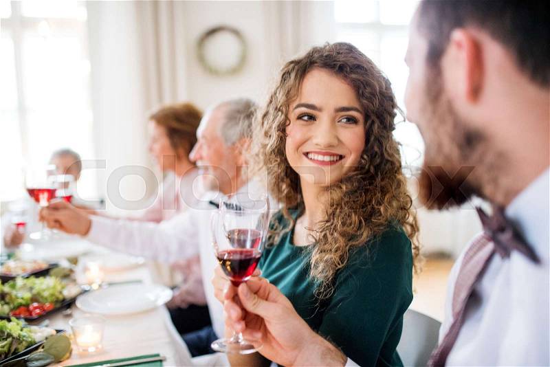 A young cheerful couple sitting at a table on a indoor birthday party, clinking glasses, stock photo