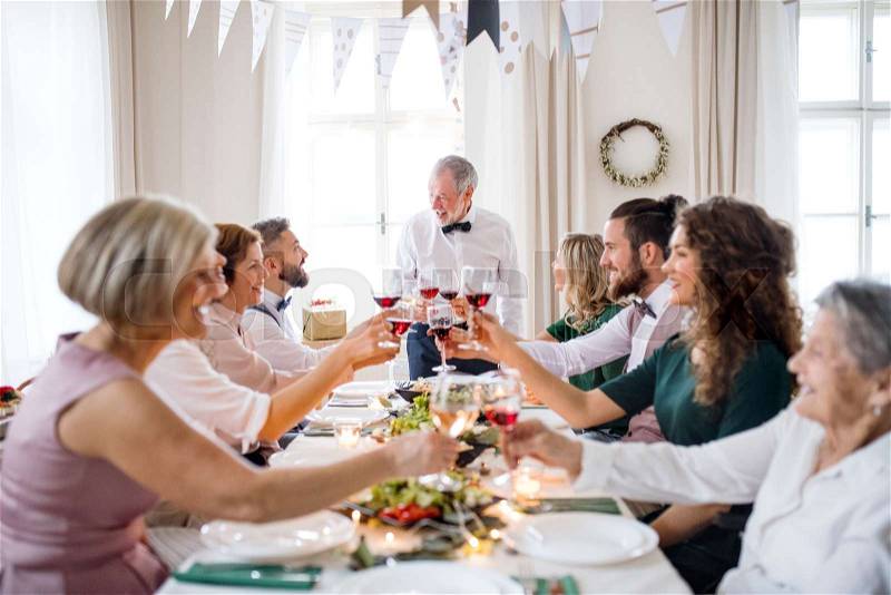 A big family sitting at a table on a indoor birthday party, clinking glasses with red wine, stock photo