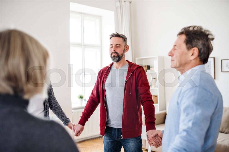 Group of people with closed eyes standing in a circle and holding hands during therapy, stock photo