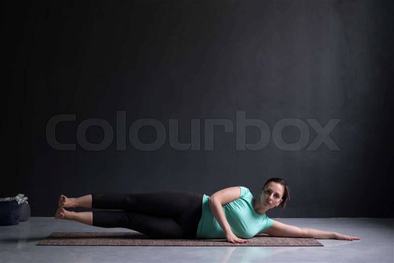 Young woman working out her side body doing side plank variation or vasisthasana yoga asana, stock photo