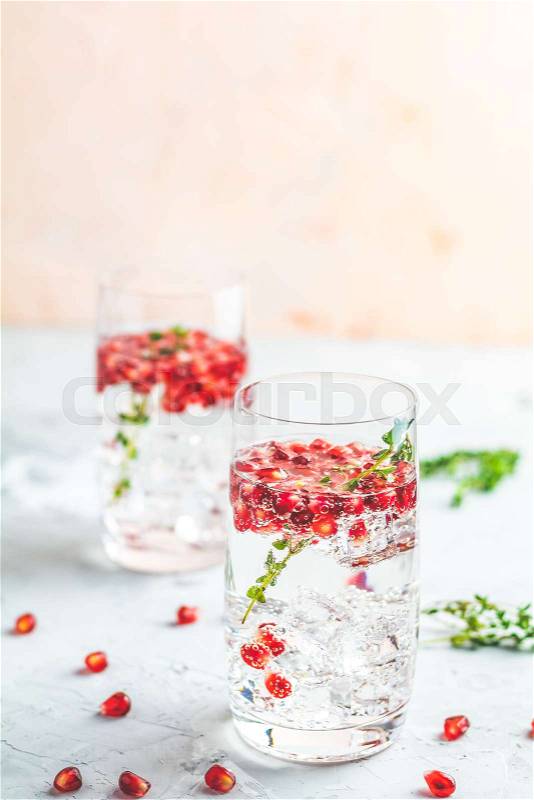 Festive drinks, gin and tonic pomegranate cocktail or detox water with ice. Selective focus, copy space for text, light gray concrete table surface, stock photo