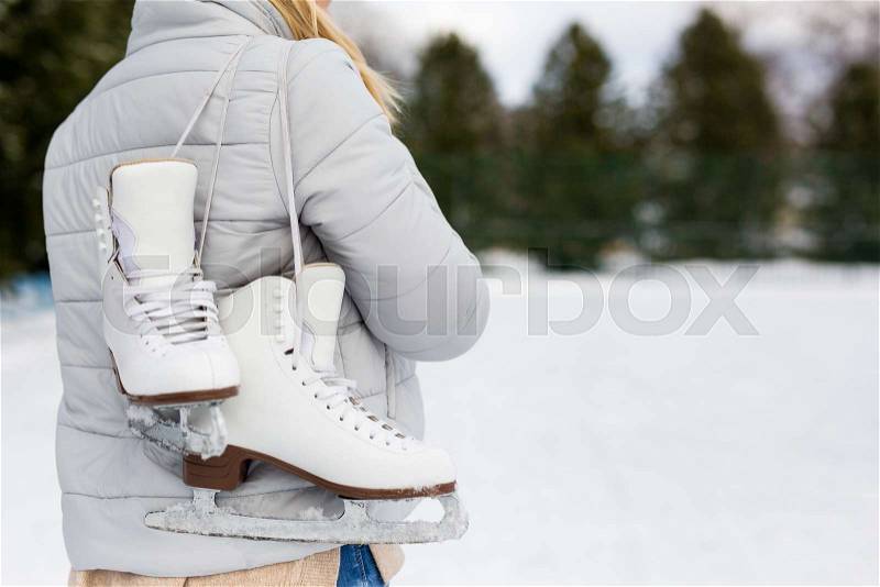 Back view of woman holding ice skates at rink in winter park, stock photo