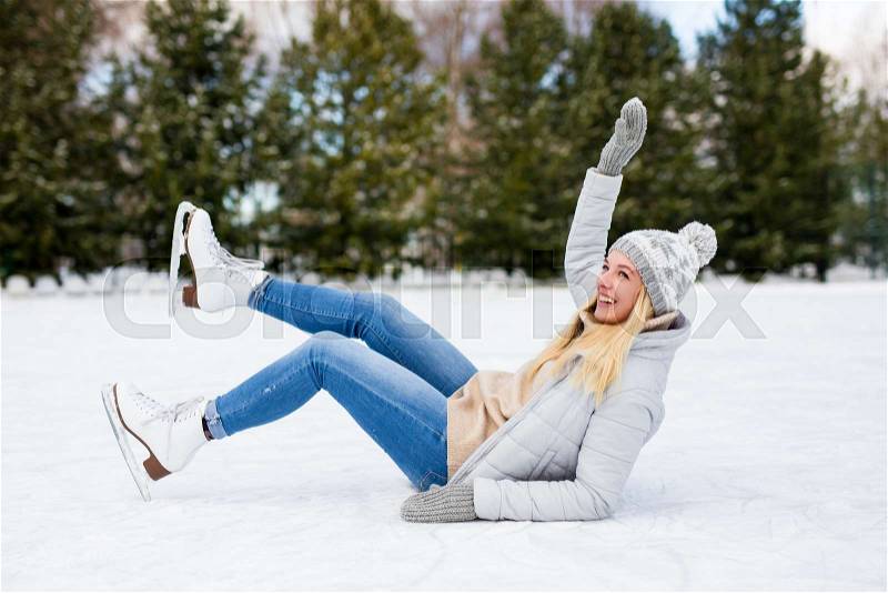 Young woman falling down while ice skating at winter rink, stock photo