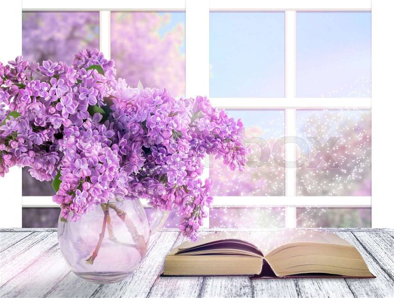 Room interior with lilac flowers in glass vase and open book on table in shabby chic style on window background, stock photo