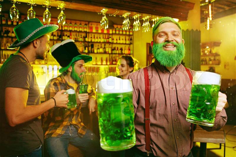 Saint Patrick\'s Day Party. Happy friends is celebrating and drinking green beer. Young men and women wearing a green hats. Pub Interior, stock photo