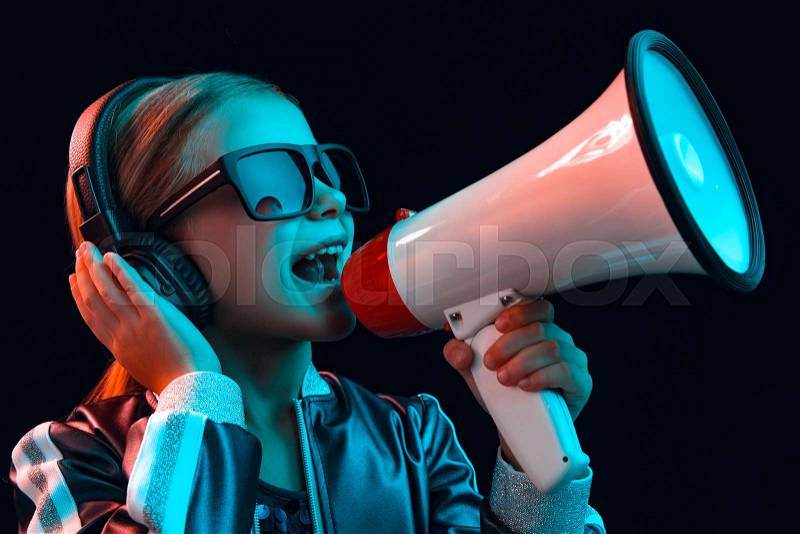 Neon portrait of young girl with headphones enjoying music and screaming to megaphone. Lifestyle of young people, human emotions, childhood, happiness concept, stock photo