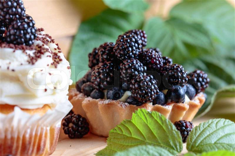 Tasty blackberry cakes with berries and cream on a wooden table, stock photo