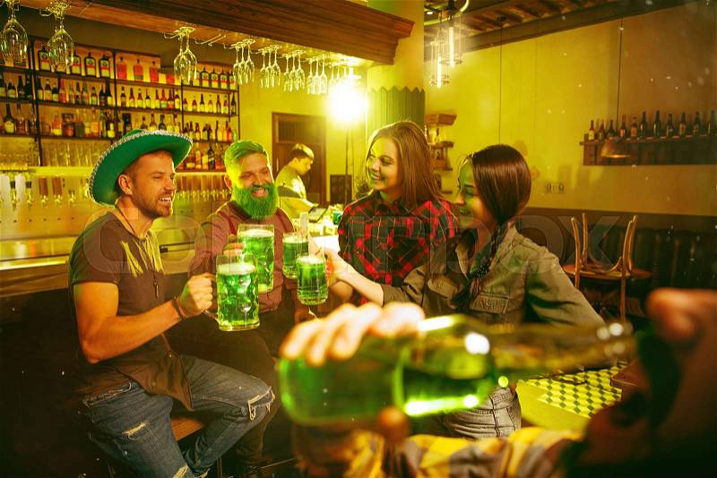 Saint Patrick\'s Day Party. Happy friends is celebrating and drinking green beer. Young men and women wearing a green hats. Pub Interior, stock photo