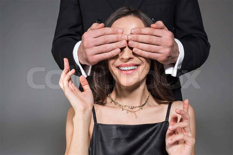 Man making surprise and closing eyes of happy girlfriend on valentines day, isolated on grey, stock photo