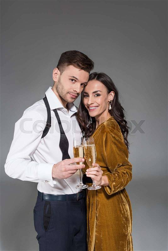 Young smiling couple hugging and holding champagne glasses isolated on grey, stock photo