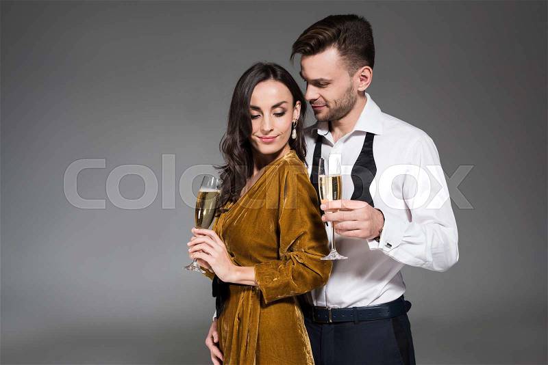 Young happy couple hugging and holding champagne glasses isolated on grey, stock photo
