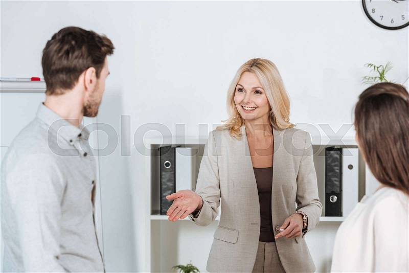 Smiling professional business mentor looking at young colleagues in office, stock photo
