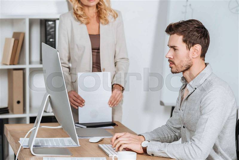 Cropped shot of business mentor holding papers and young businessman using desktop computer in office , stock photo