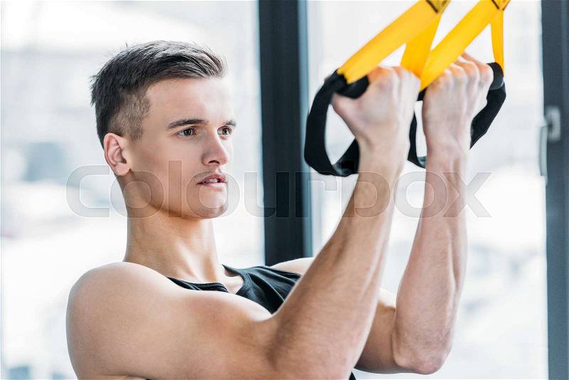 Handsome muscular young man exercising with suspension straps in gym , stock photo