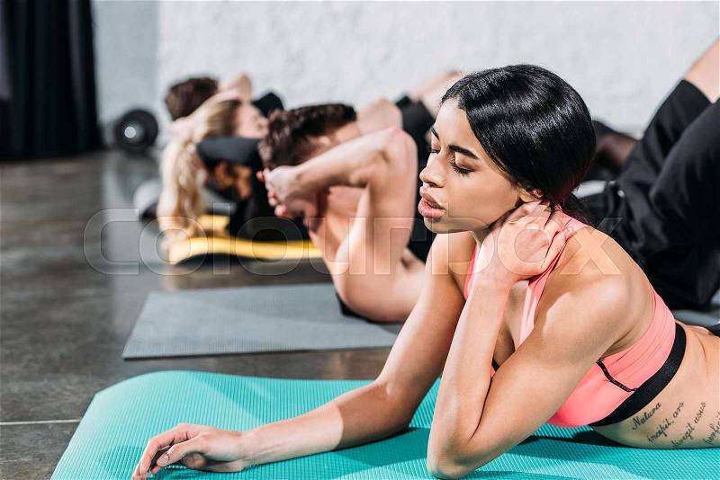 Tired african american girl touching neck while exercising on yoga mat in gym, stock photo
