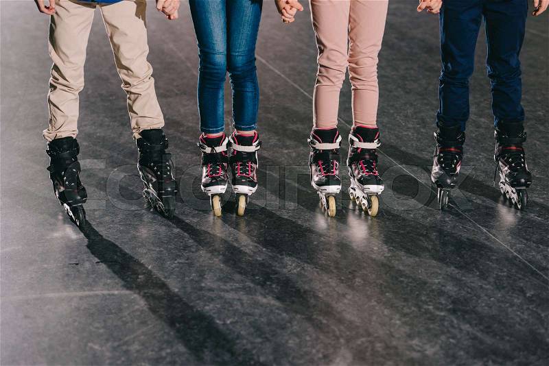 Partial view of children in roller skates standing in roller rink and holding hands, stock photo