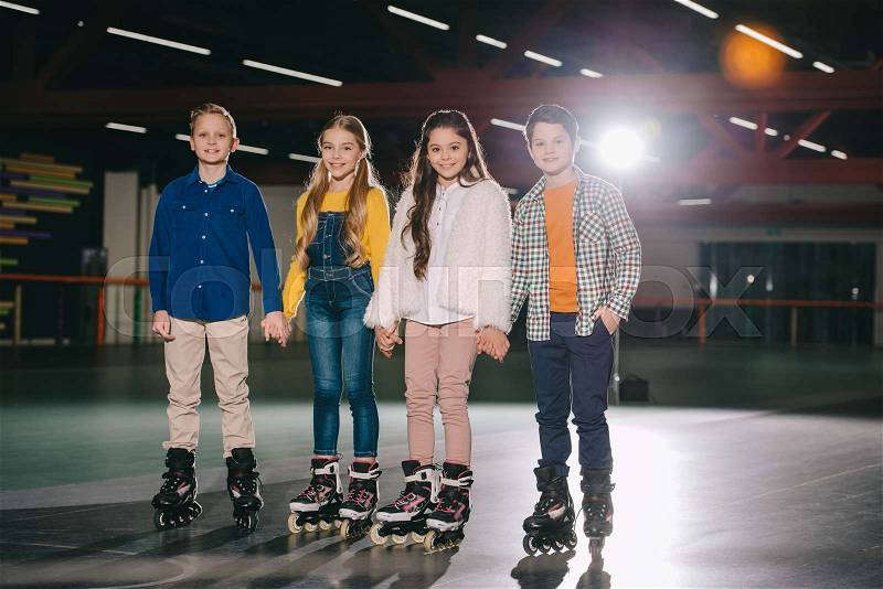 Cute smiling children in roller skates standing on spacious roller rink, stock photo