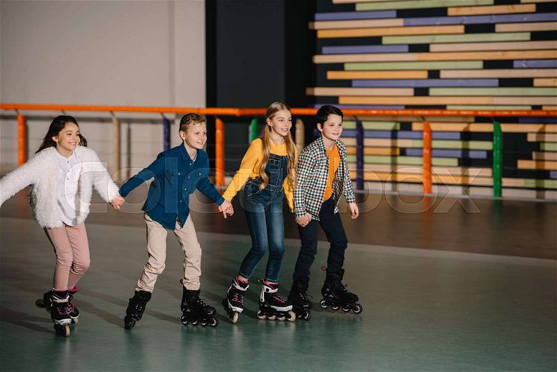 Group of smiling children skating in roller rink with holding hands, stock photo
