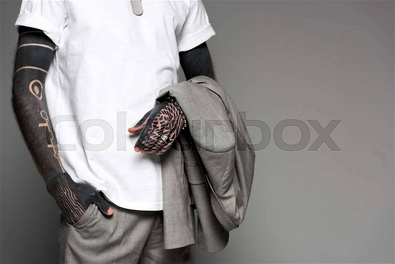 Cropped shot of tattooed man in white t-shirt holding suit jacket isolated on grey, stock photo