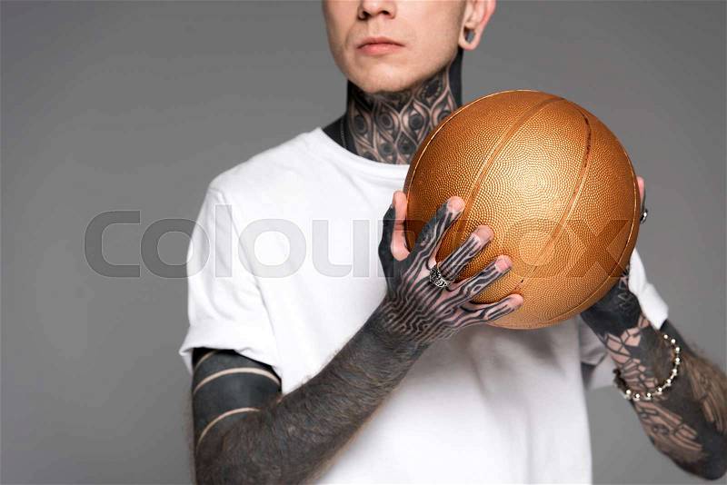 Cropped shot of tattooed man in white t-shirt holding golden basketball ball isolated on grey, stock photo