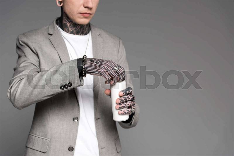 Cropped shot of tattooed man in suit jacket opening aluminum can isolated on grey, stock photo