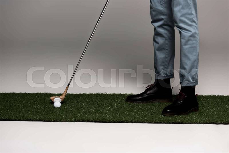 Low section of man in jeans and leather boots playing golf on artificial grass on grey, stock photo