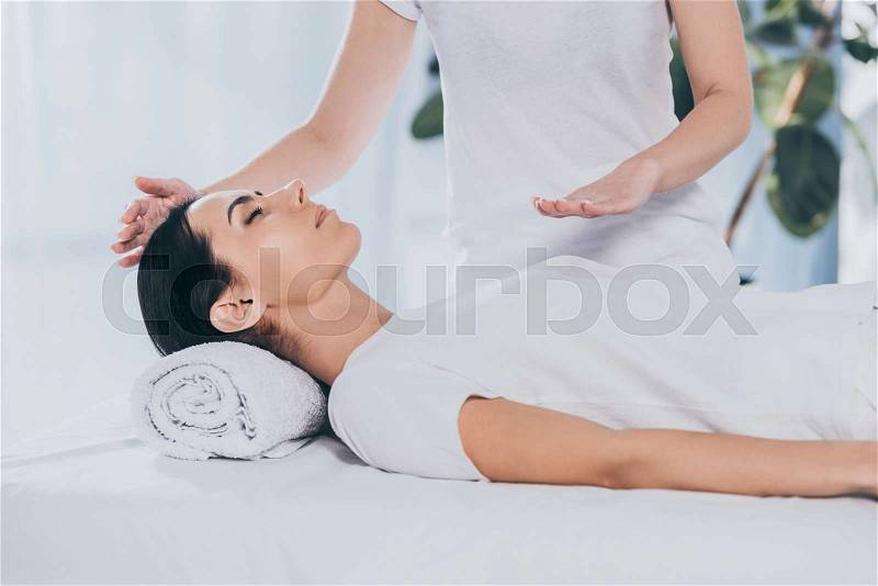 Peaceful young woman receiving reiki healing treatment on head and chest, stock photo