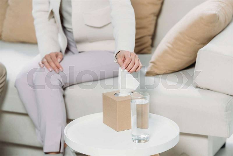 Cropped shot of woman sitting on couch and holding paper tissue in psychotherapist office, stock photo