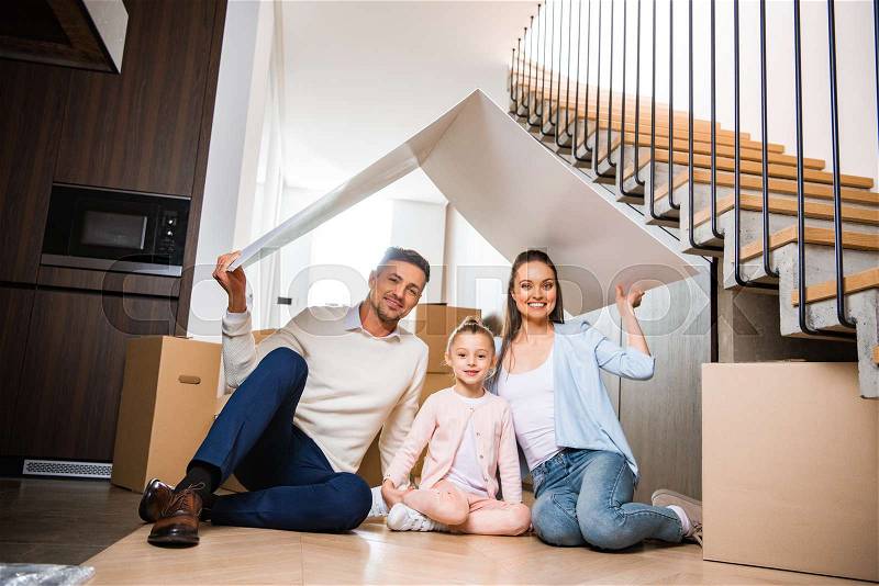 Happy family sitting under paper roof and smiling in new home , stock photo