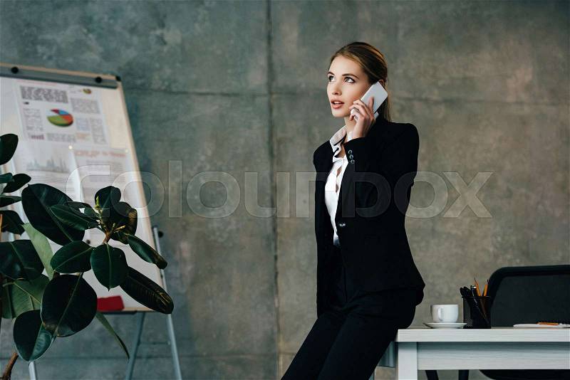 Young businesswoman stands by workplace and talking on smartphone , stock photo