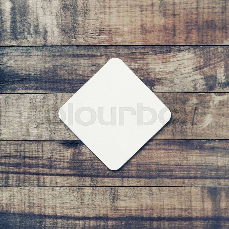 Blank square beer coaster on vintage wooden background. Flat lay, stock photo