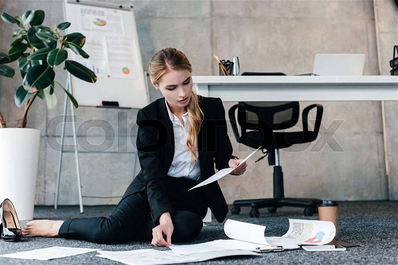 Barefoot businesswoman sitting on floor and reading document, stock photo
