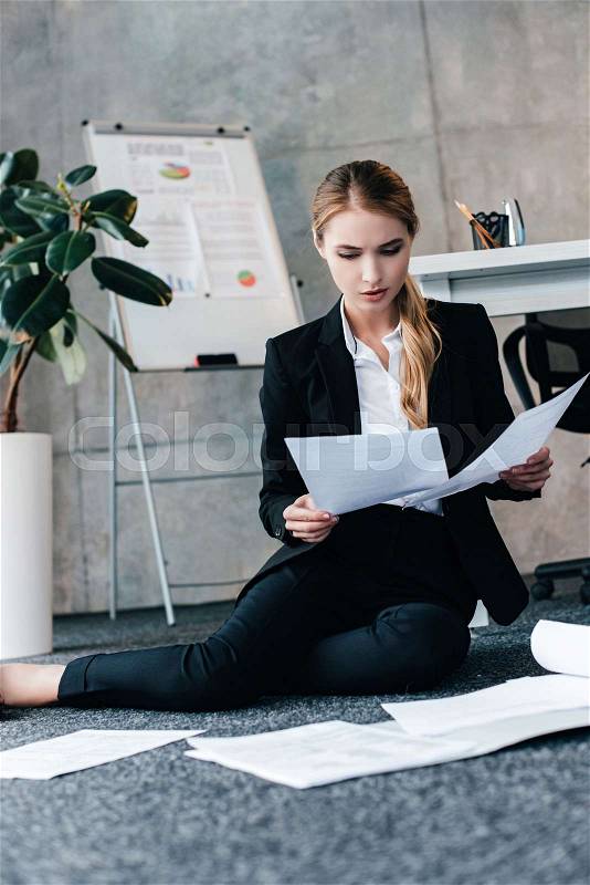 Barefoot businesswoman sitting on floor and reading document, stock photo
