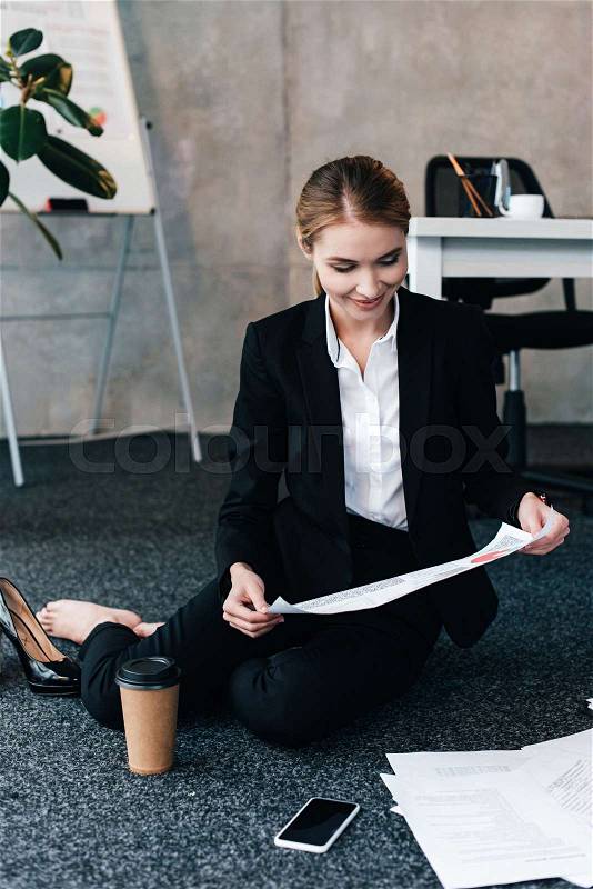 Selective focus of barefoot businesswoman sitting on floor and reading document, stock photo