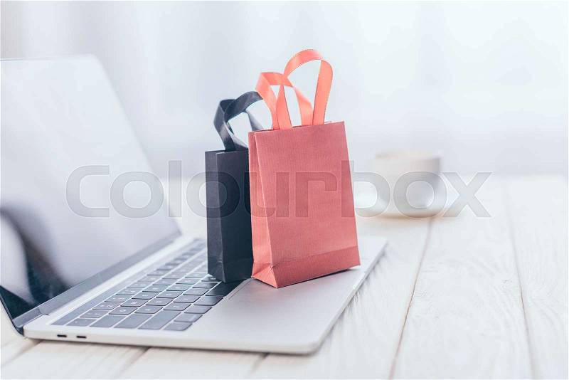 Selective focus of small shopping bags on laptop with cup on background, stock photo