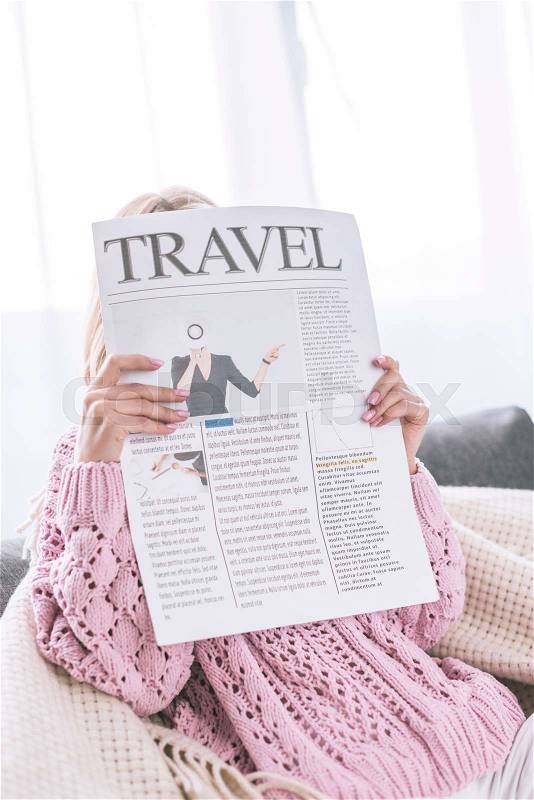 Woman reading travel newspaper while sitting at home, stock photo