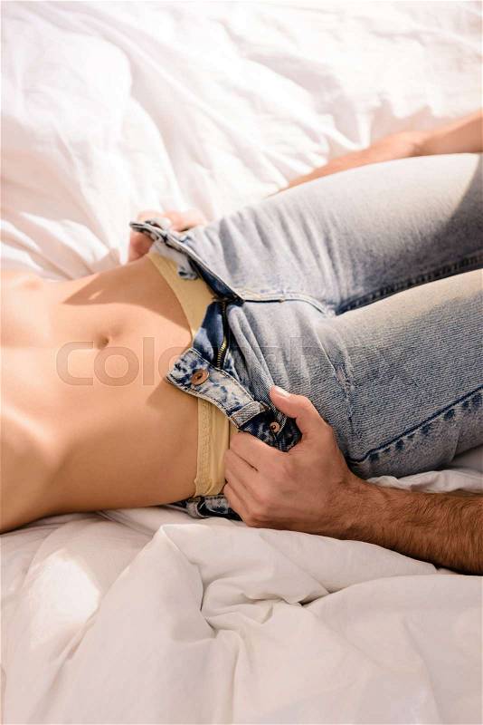 Cropped view of man undressing woman on bed, stock photo
