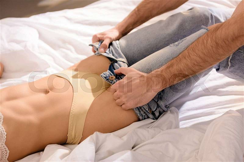 Cropped view of man undressing woman on bed, stock photo