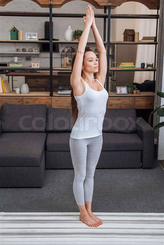 Beautiful young woman practicing yoga pose at home in living room, stock photo