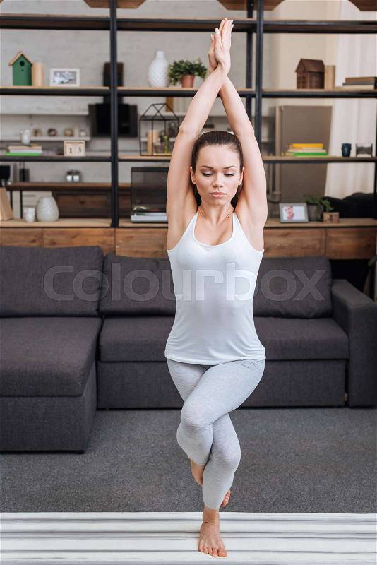 Young woman practicing eagle pose at home in living room, stock photo
