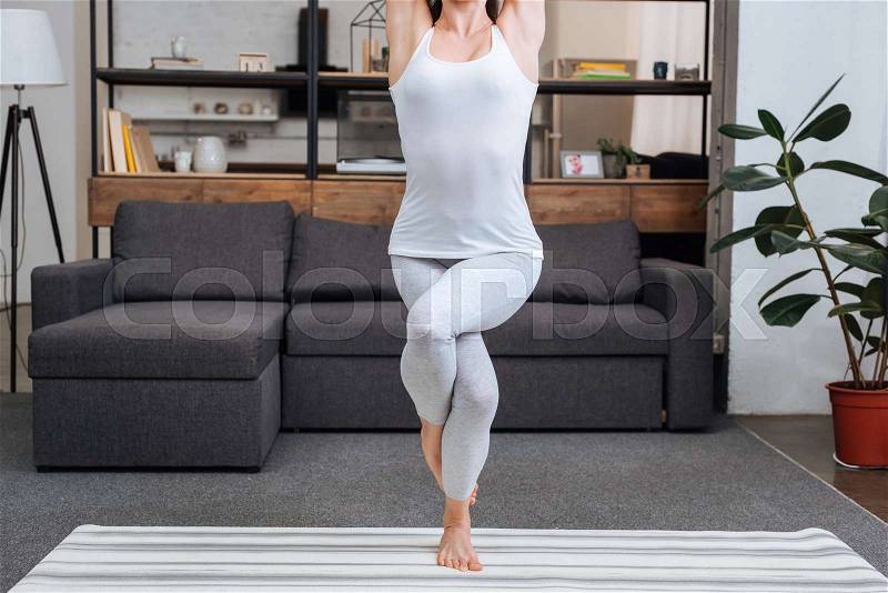 Cropped view of woman practicing eagle pose at home in living room, stock photo
