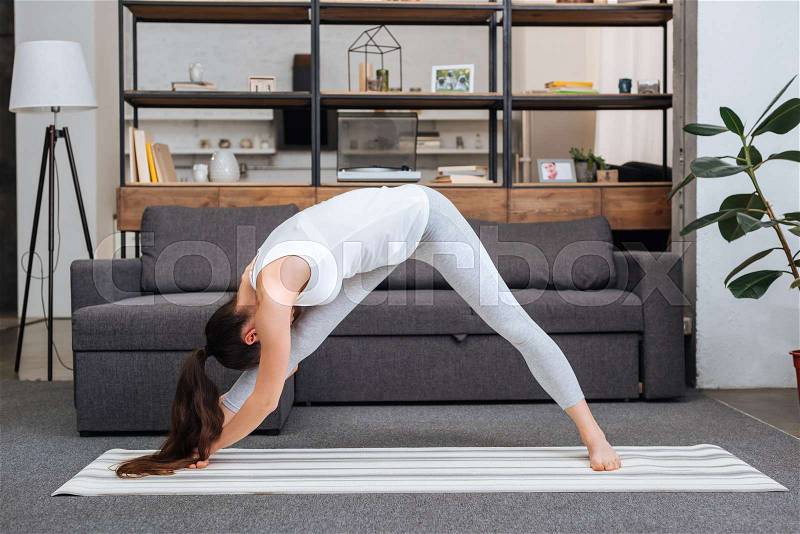 Young woman practicing intense side stretch pose at home in living room, stock photo
