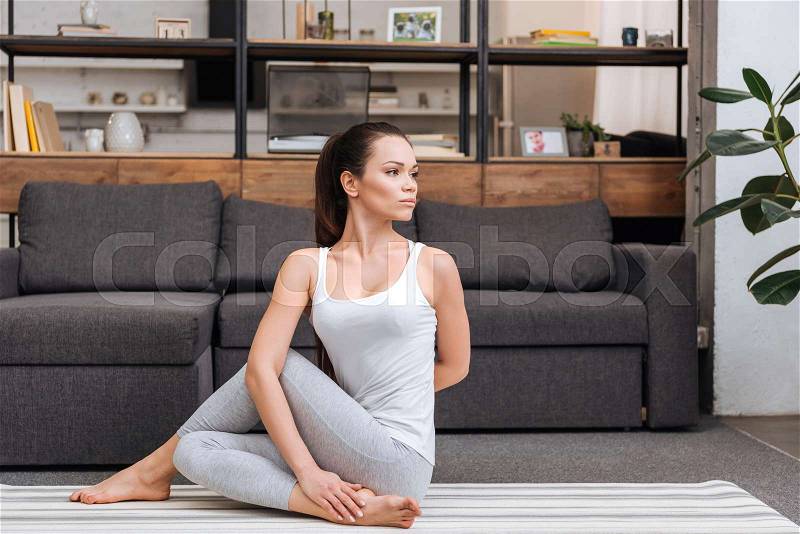 Woman practicing ardha matsyendrasana at home in living room, stock photo