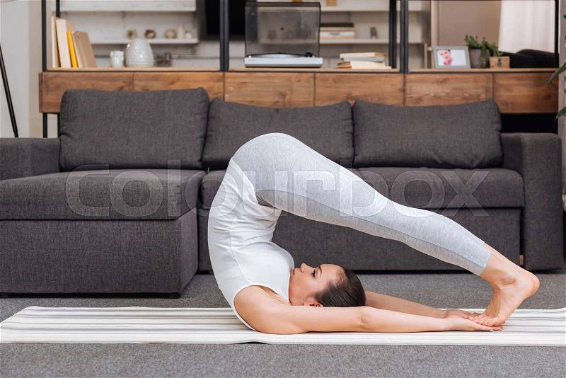 Woman practicing boat pose at home in living room, stock photo