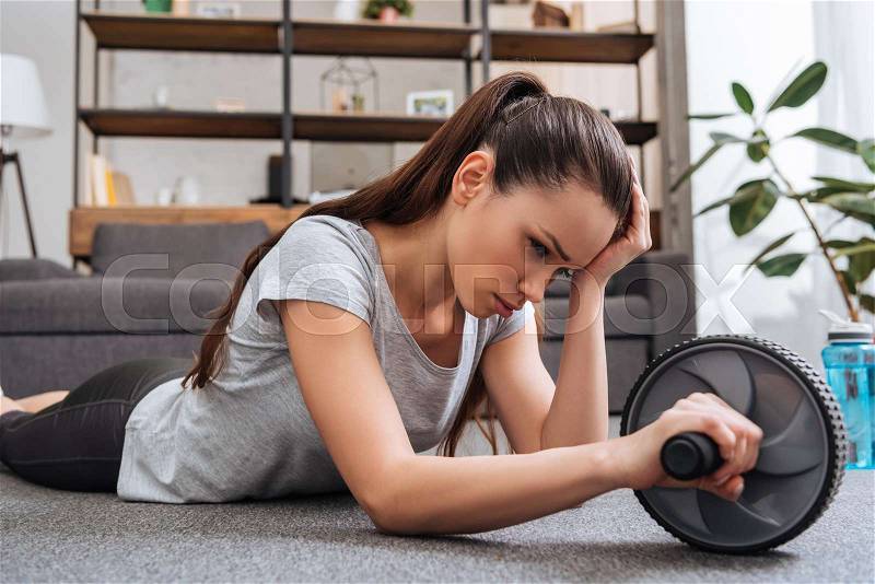Exhausted sportswoman training with ab wheel at home, stock photo