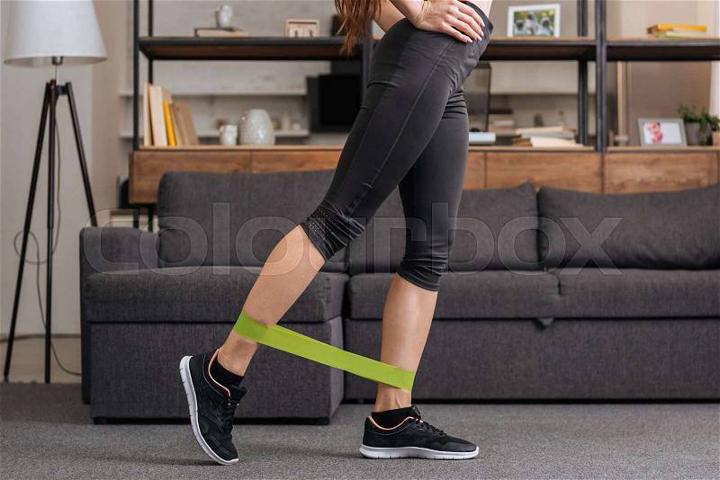 Low section of sportswoman training with resistance band at home in living room, stock photo