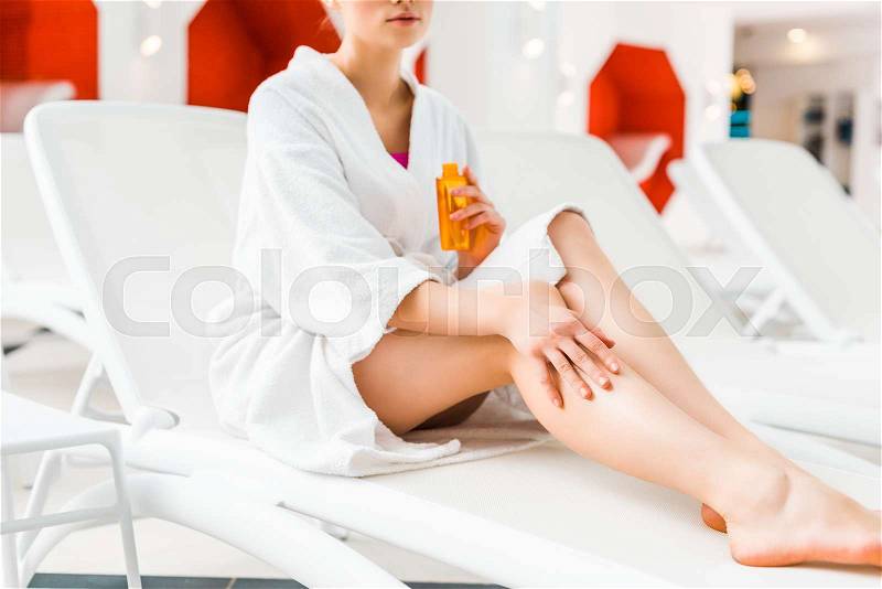 Cropped view of woman applying body oil on leg while sitting on deck chair , stock photo
