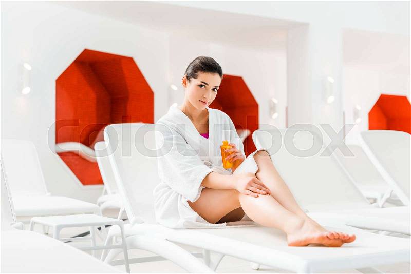 Beautiful woman applying body oil on leg while holding bottle , stock photo