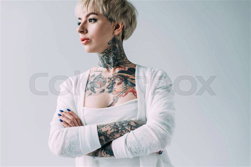 Attractive woman with tattoos standing with crossed arms isolated on grey, stock photo