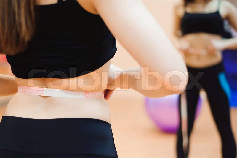 Young slim woman measuring waist using the tape measure, stock photo